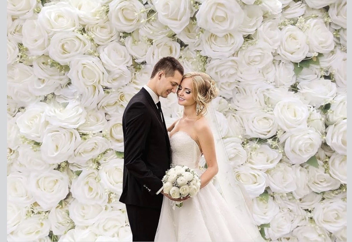 The White Flower backdrop — a bride and groom standing forehead to forehead in front of a full wall of white roses